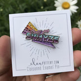 A hand holding a 'Crazy for Swayze' enamel pin with a floral pattern in front of a card that reads 'elantransfers.com Cloisoné Enamel Pin'.